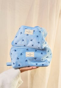 Bolsas de viaje de tela suave y azul con patrones de lazo bordados, que presentan cierres de cremallera y etiquetas que dicen "THE FLAT LAY CO. LONDON."