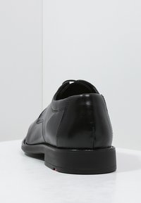 Black leather shoe with a smooth finish, rounded toe, and a low black sole. Features subtle stitching details and a slight heel.