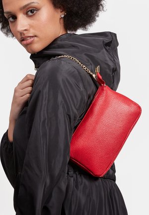 Geantă de umăr din piele texturată roșie, cu o curea lanț aurie. Formă dreptunghiulară, finisaj neted, prevăzută cu închidere cu fermoar și o etichetă din material textil.