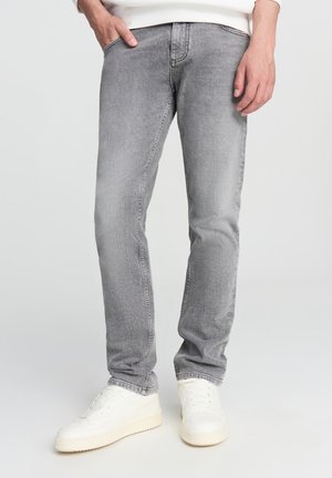 Jeans in denim grigio con vestibilità slim, caratterizzati da cinque tasche, un leggero sbiadimento e gamba leggermente affusolata, abbinati a sneaker bianche.