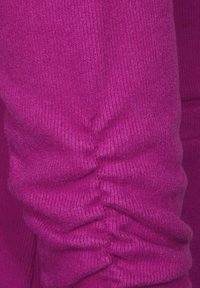 Fuchsie, texturovaná pletenina s nabíranými detaily podél švu, vytvářející jemný proužkový efekt. Měkký a elastický povrch.
