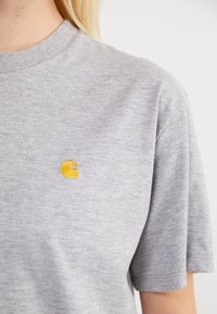 Gray cotton t-shirt with a round neckline and short sleeves, featuring a small yellow embroidered logo on the chest.