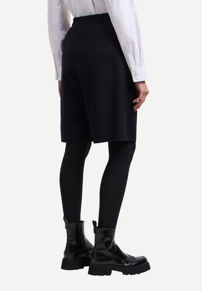 Pantaloncini neri su misura con cintura elastica, abbinati a collant neri e stivali alla caviglia lucidi. Tessuto liscio con un design strutturato.