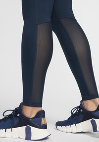 Marina leggings med meshnätpaneler, sömlös design och sydda detaljer, tillsammans med marina sportskor med vit sula och varumärkeslogotyp.