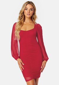 Rode bodycon jurk met een vierkante halslijn, doorschijnende lange mouwen en gerimpelde details langs de zijkanten. Soepele stofstructuur.