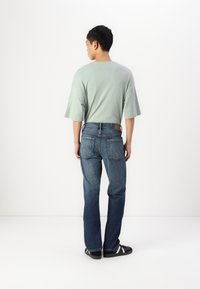 Mátově zelené oversized tričko, středně těžká látka; modré denimové džíny s rovný střih, klasický pětikapsový design a tmavé akcenty.