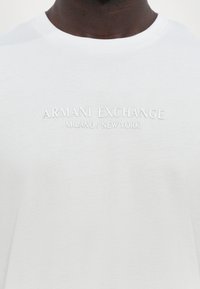 Hvit bomulls T-skjorte med preget tekst "ARMANI EXCHANGE MILANO / NEW YORK" på fronten. Rund hals og kortermet design.