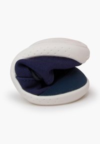 Zapato flexible con una suela de goma blanca y parte superior de textil azul marino. El zapato está parcialmente enrollado, mostrando su suave construcción.