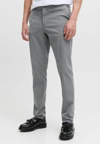 Pantalones grises de corte slim con una textura suave, que cuentan con presillas para cinturón, bolsillos laterales y un acabado limpio. Combinados con zapatos negros brillantes.