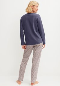 Langärmeliges marineblaues Oberteil mit Rundhalsausschnitt, kombiniert mit gemusterten beigen und marineblauen Hosen mit geometrischem Design. Lockerer Schnitt, weicher Stoff.