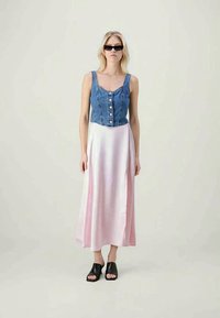 Jeans crop top με κουμπί, συνδυασμένο με μια ρέουσα ροζ σατέν maxi φούστα. Διαθέτει απλά μαύρα σανδάλια.