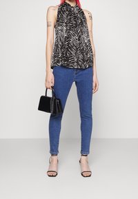 Czarna i biała bluzka w print zebry bez rękawów z gromadzonym dekoltem, w połączeniu z niebieskimi wąskimi dżinsami i małą czarną torebką. Czarne sandały na obcasie.