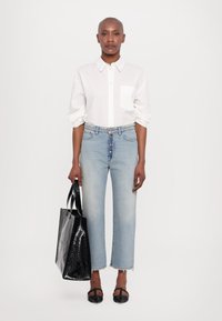 Camicia bianca con bottone sulla parte anteriore e tasca sul petto, jeans a vita alta blu chiaro, borsa a tracolla nera in vernice e scarpe nere basse con cinturini.