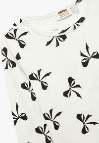 Witte katoenen shirt met zwart strikpatroon, voorzien van een geribbelde textuur en een ronde hals. Label zegt "Katton KIDS 6-7Y, 116-122CM."