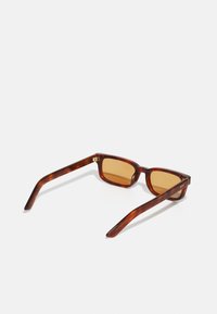 Gafas de sol carey marrón con montura rectangular y lentes de tono marrón. Presentan detalles dorados en la patilla. Acabado de plástico suave.