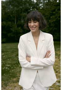 Witte blazer met een getailleerde pasvorm, zachte stof, met gelapte revers en lange mouwen. Gedeeld over een bijpassend top, met een natuurlijke buitensetting.