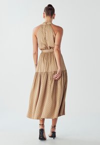 Béžové midi šaty s bodkami zo ľahkej tkaniny, s halter krkom, zúženým pásom a vrstvenou sukňou; v kombinácii s čiernymi lodičkami na členkových remienkoch.