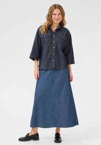 Denim krekls ar pogu aizdari, divām krūšu kabatām un trim ceturtdaļām piedurknēm, apvienots ar garu, zilu džinsu svārku un melniem mokasīniem.