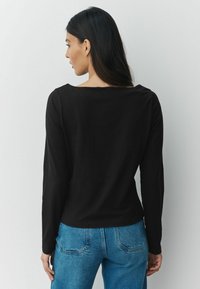 Hosszú ujjú fekete felső, kerek hátkivágással, magas derekú kék farmernadrággal párosítva. Sima textúra, egyszerű dizájn, nincsenek figyelemfelkeltő minták.