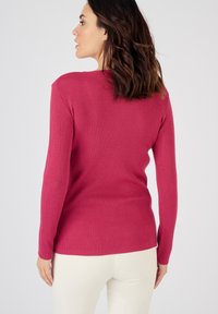 Haut côtelé en magenta, design ajusté avec des manches longues. Le tissu semble doux avec une finition texturée. Modèle portant un pantalon clair.