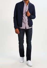 Námořnická bomber bunda přes kostkovanou košili, doplněná tmavými džínami a bílými teniskami. Důraz na elegantní design a pohodlný střih.