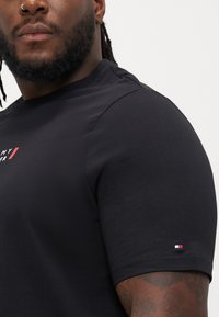 Μαύρο κοντομάνικο μπλουζάκι φτιαγμένο από βαμβάκι. Διαθέτει Λογότυπο σε λευκό και κόκκινο χρώμα στο στήθος, με μια μικρή τριχρωμία στον μανίκι.