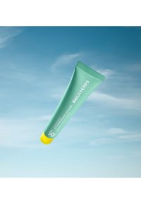 Grön tub med solskyddskräm med gul kork; märkt "BIOTHERM," SPF 50; slät konsistens, lätt design, lämplig för daglig användning.