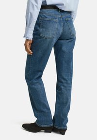 Blå denimjeans med rak benfitting, som har två bakfickor och en medeltvättad yta, tillsammans med mörka skor.