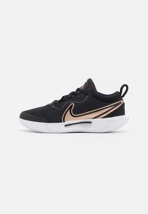Chaussure de sport basse noire avec le logo Nike en or rose, semelle blanche, lacets noirs et une languette à l'arrière, présentée sur un fond blanc.