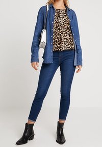 Chemise en denim, haut imprimé animal, jean skinny bleu foncé, bottines noires ; avec un petit sac à main à bandoulière en chaîne argentée.