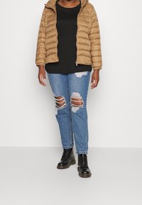 Hnědá prošitá bunda s kapucí, černý top, potrhané světle modré džíny a černé šněrovací boty. Důraz na texturu a ležérní styl.