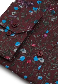Materiał w kwiaty w kolorze burgundowym z niebieskimi, różowymi i szarymi kwiatami. Posiada dwie ciemne guziki na klapie oraz miękką fakturę.
