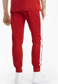 Red jogger pants featuring white side stripes, made from a smooth fabric with elastic cuffs and a relaxed fit at the ankles.