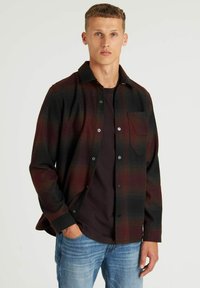 Geruit flanellen shirt in donkerrood en zwart, met een knoopsluiting, één borstzak en een relaxte pasvorm over een donker T-shirt.