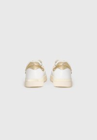 Sneakers bianchi in pelle con forma arrotondata, caratterizzati da un accento dorato sul tallone e suole color crema. Texture liscia, design minimal.