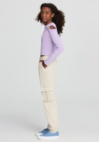 Liliowy top z długimi rękawami i wycięciami na ramionach, w zestawieniu z kremowymi spodniami cargo z bocznymi kieszeniami oraz niebieskimi trampkami z białymi podeszwami.