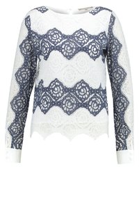 Top in pizzo a maniche lunghe con orlo a scallop, caratterizzato da motivi floreali alternati in blu navy e bianco, e polsini bianchi con bottoni.