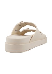 Beige rubberen slip-on sandaal met een dikke zool, open teen en breed kruisbandontwerp. Textuurafwerking en ronde klinknageldetails op de banden.