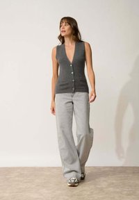 Cárdigan gris sin mangas con escote en V profundo y cierre de cinco botones, combinado con jeans de pierna ancha gris claro y zapatillas con un diseño estampado.