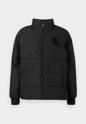 Czarna kurtka puchowa z wysokim kołnierzem, zamkiem błyskawicznym i elastycznymi mankietami. Na piersi widoczne jest wyraźne czarne logo.