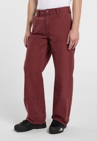 Pantaloni da lavoro bordeaux realizzati in tessuto resistente, caratterizzati da gambe dritte, molteplici tasche e dettagli in metallo per la funzionalità.