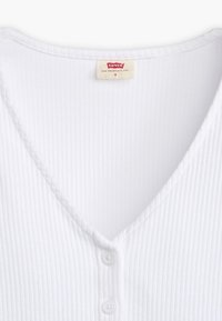 Bílý žebrovaný top na ramínka s výstřihem do V a třemi knoflíky vpředu. Vyroben z měkké tkaniny, má jemnou strukturu po celé ploše. Velikost S.