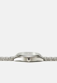 Montre en acier inoxydable avec un boîtier rond, une lunette lisse et un bracelet à maillons en métal. Cadran en verre clair avec des index horaires simples.