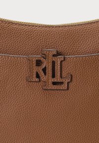 Saco de couro castanho com superfície texturizada, apresentando um logo RL em bronze. Detalhe de fecho éclair no topo, com costura contrastante visível no corpo.