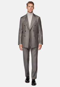 Gray double-breasted suit with a textured finish, paired with a light turtleneck. Black dress shoes complete the formal look.