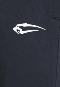 Weißes stilisiertes Pandakopf-Logo auf dunklem Stoff, in der Nähe einer Naht auf Kleidung positioniert.