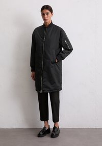 Zwarte bomberjack met een voorrits, ribgebreide manchetten, zijzakken en een stijlvolle, gladde textuur. Draag het over zwarte cropped broeken en loafers.