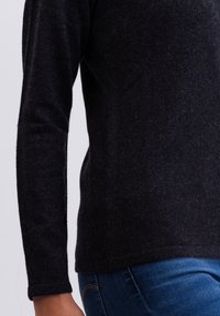 Maglione nero a maniche lunghe realizzato in materiale morbido. Presenta un orlo inferiore arrotondato e maniche aderenti, abbinato a jeans in denim blu.