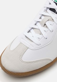 Witte sneaker met een leren bovenwerk en suède accenten, ronde neusontwerp en een gestructureerde rubberen zool van gum. Witte veters maken de look compleet.