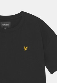 Schwarzes Baumwoll-T-Shirt mit Rundhalsausschnitt. Mit einem kleinen, gelben gestickten Adler-Logo auf der Brust. Einfaches Design, kurze Ärmel.